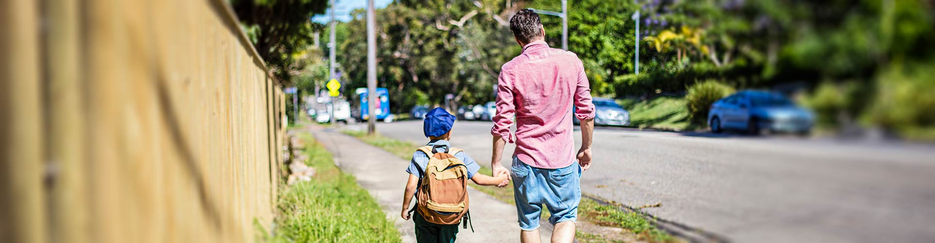 School boy walks hand in hand with father on side of street