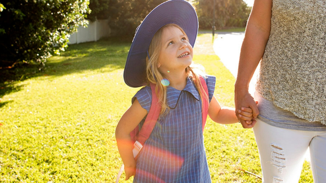 Primary school-age girl in school uniform holding hands with and looking up at her mother