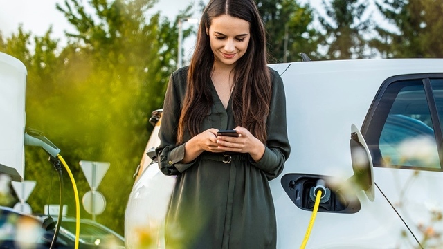 Someone smiles at their phone as they wait for their EV to charge in the background