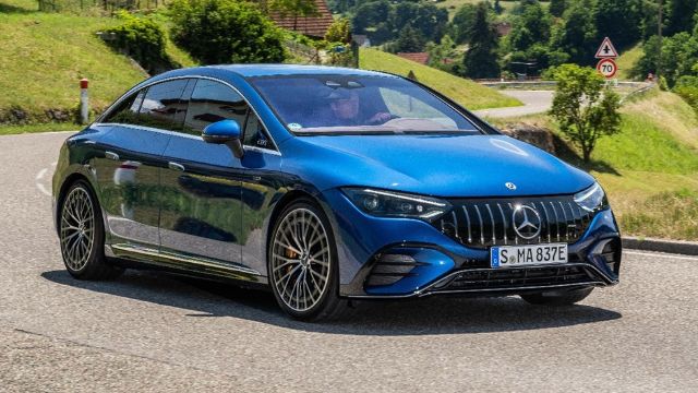 A blue Mercedes EV drives along a picturesque country road