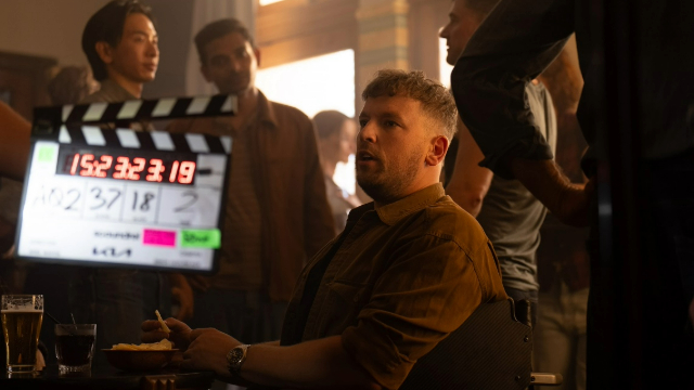 Wheelchair tennis champion Dylan Alcott in a dimly lit room with lots of people around and a digital clapperboard being held up near him.