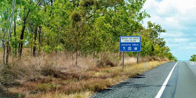 A blue driver reviver road sign next to a country road
