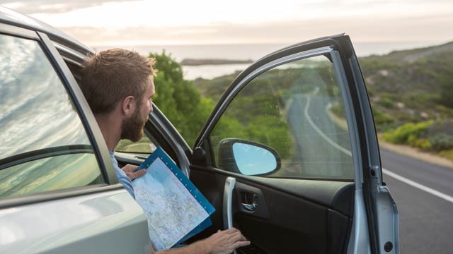 Man holding a map in the a car by the side of the road