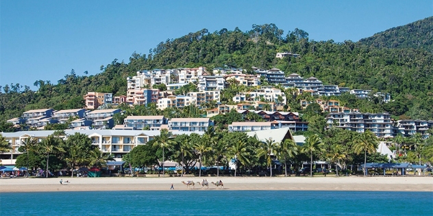 view from the sea towards land showing buildings nestled into the hillside and camel rides on the beach