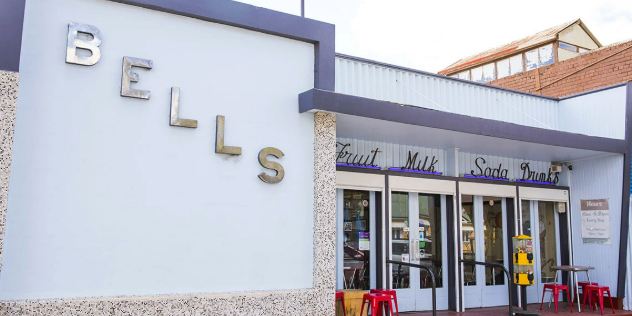  An art deco style lavender and purple trimmed shopfront, with the word Bells written diagonally across it, with tables outside.