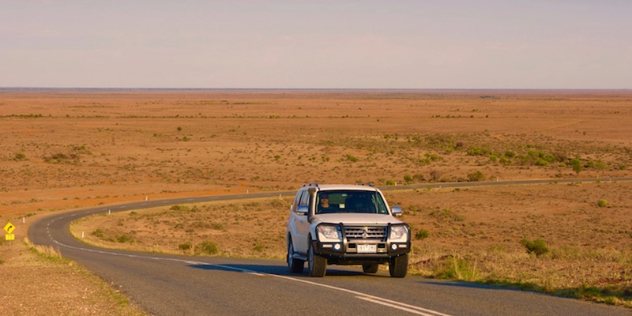 white four-wheel drive vehicle on a road winding through flat dry grasslands