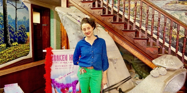 inside the pub, owner Esther wears a mid-blue shirt and light green trousers and stands next to a giant high heel prop from the movie priscilla queen of the desert