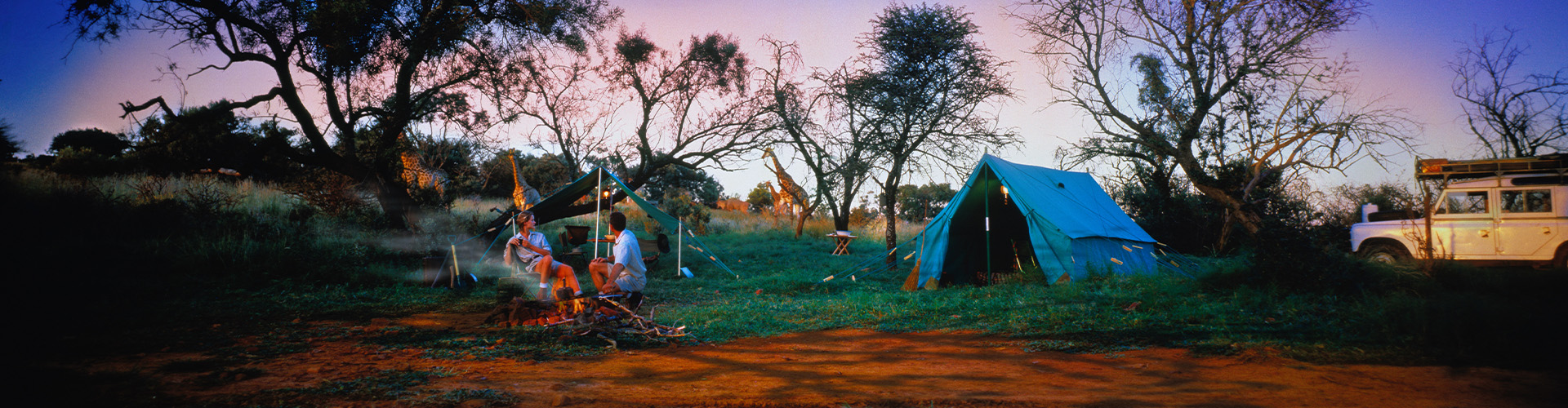 Two people at a campfire with a tent and car in the background