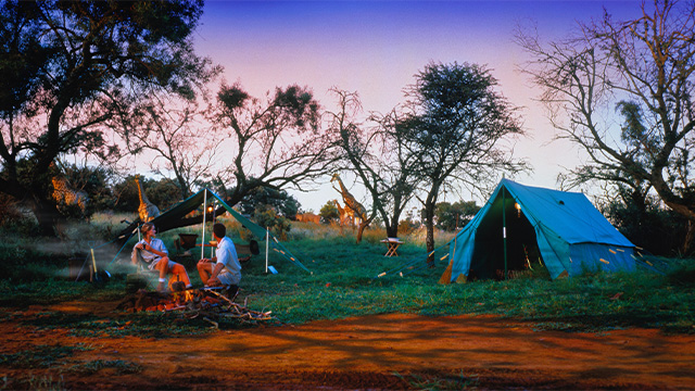 Two people at a campfire with a tent and car in the background