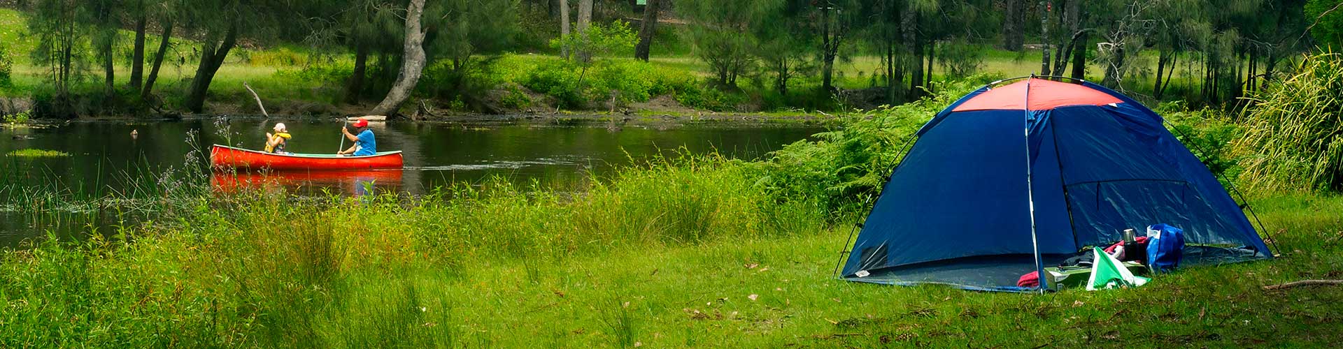 Camping tent setup while people are riding a kayak along Hacking river in Royal National Park