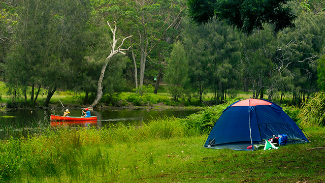 Camping tent setup while people are riding a kayak along Hacking river in Royal National Park