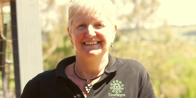  A smiling woman with short, white hair, standing outside wearing a t-shirt with Courabya Wines written on it.