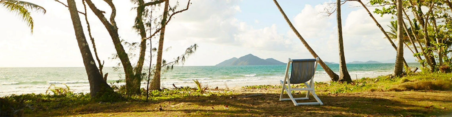 chair-on-beach-cairns-qld-1920x500 One cloth folding chair in front of a sunny, tropical beach, with mountains or an island visible in the distance.