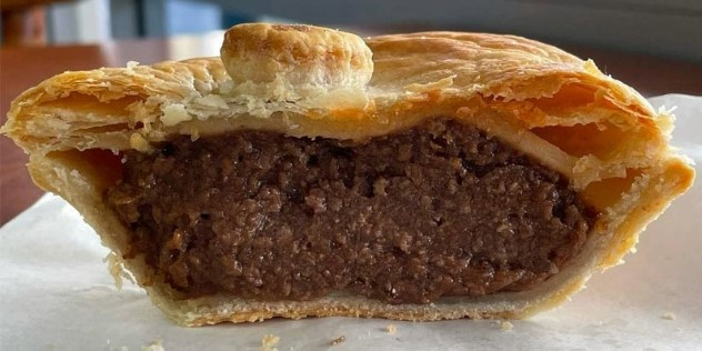 A close up of a flaky, pastry meat pie cut in half to expose dense, gooey looking meat filling, at Kens Humble pie café. 