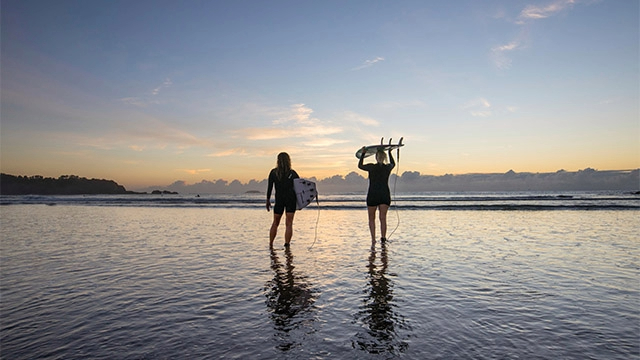 surfers look out to sea standing in water on Coffs Harbour beach