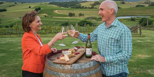 man and woman enjoying wine and a cheese platter outside with a view of vineyards in the background