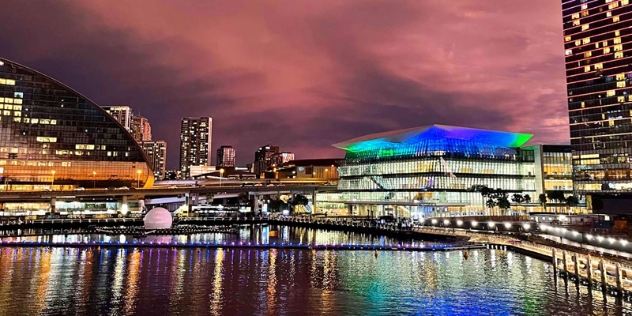 lights from multistorey buildings surrounding darling harbour are reflected in the still water