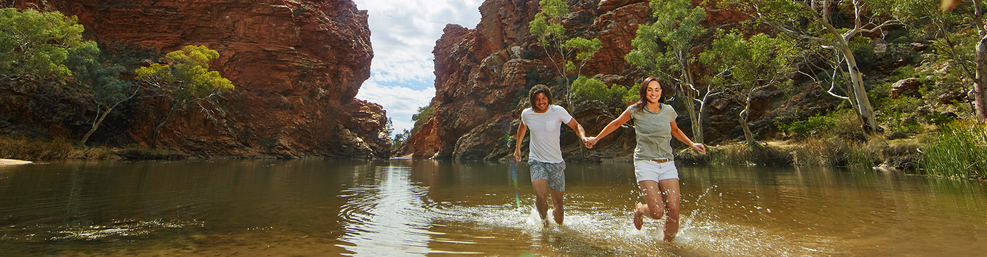 a man and a woman holding hands and frollicking in the shallows of a creek