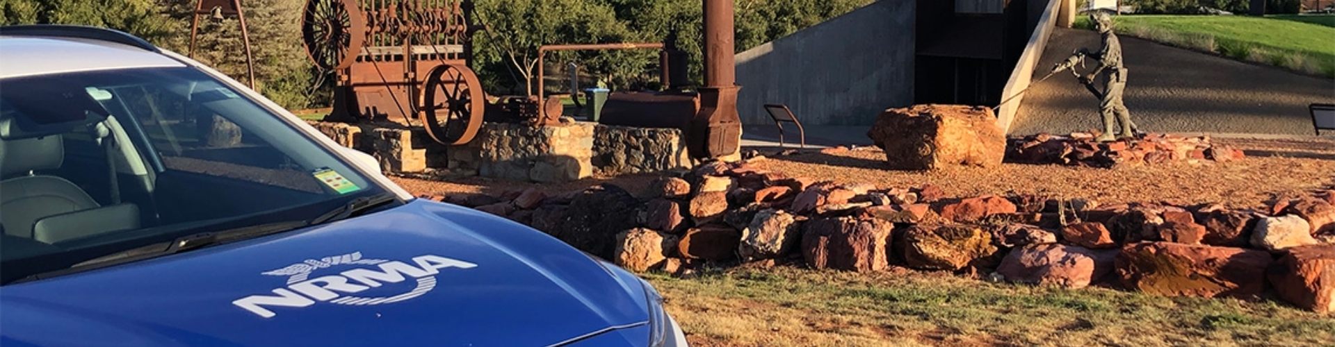 ev Cobar Miners Heritage Park NSW NRMA electric vehicle parked next to exhibit of old machinery and a sculpture of a miner