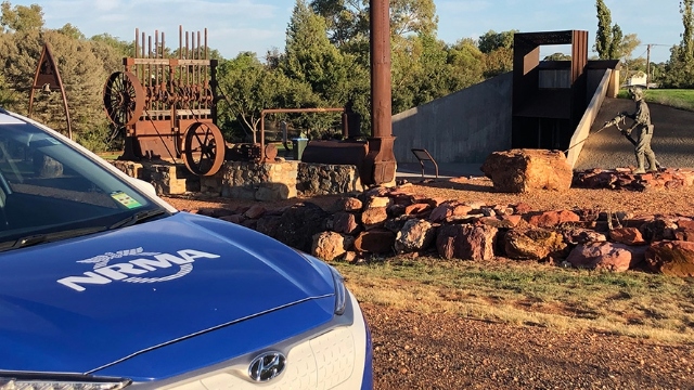 NRMA electric vehicle parked next to exhibit of old machinery and a sculpture of a miner