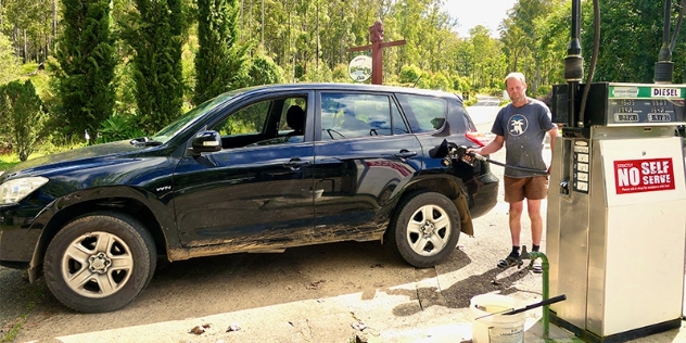 owner Gary at Gingers Creek service station filling up a black car with fuel next to a sign that says No self serve