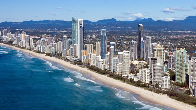 A panoramic view of Gold Coast beach and city skyline, with mountains on the horizon.
