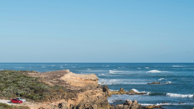 arial view of the coastline and ocean with a red and white car parked at the lookout