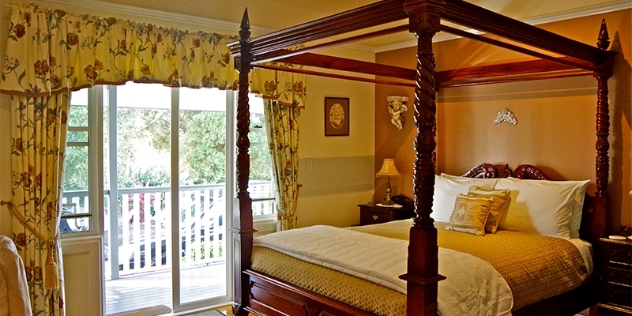 pretty bedroom with rose patterned curtains and a four-poster bed with multiple cushions and pillows