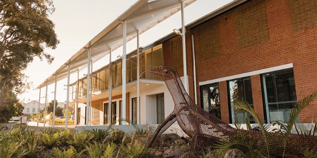 wire garden sculpture of lizard in the gardens in front of a modern red brick building with large windows and a white sunshade