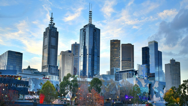 The Melbourne city's business district skyscrapers, framed by trees and blue sky.