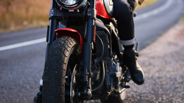 Close up of the front of a motorbike parked on a roadside with a biker's boot on the kickstand ready to take off.