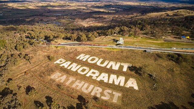 An aerial view of the words Mount Panorama Bathurts mowed into the grass on a sunny hillside next to a road.