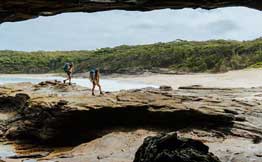 Two people walk on rocky shoreline seen from cave