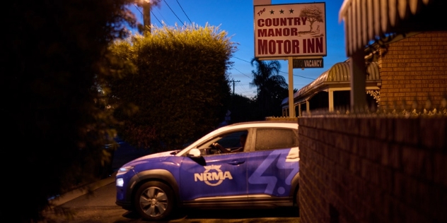 blue and white NRMA electric vehicle driving past a sign for the Country Manor Motor Inn