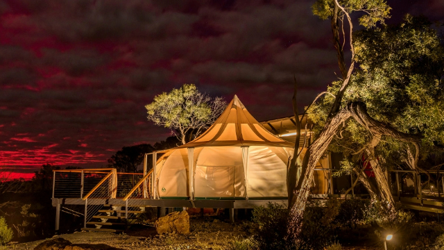 A large canvas tent on a wooden verandah at sunset, surrounded by gum trees.