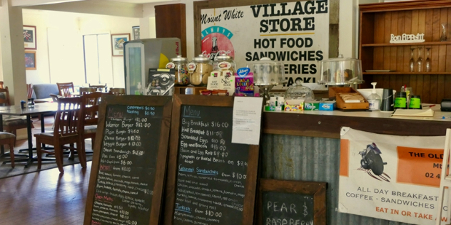  A wood and corrugated iron cafe counter with chalk board menus laid against it and vintage candy dishes and covered cakes on top.