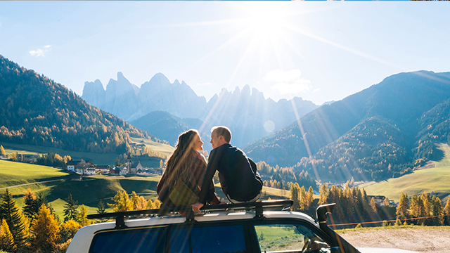 TitleCouple sit on car rooftop looking at mountains in the distance
