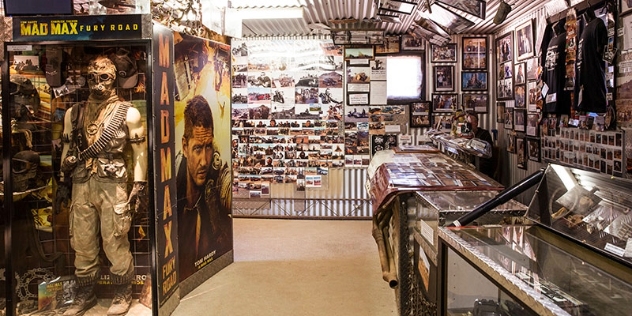 photographs and posters cover the walls and display cases show film props and costumes from the mad max films