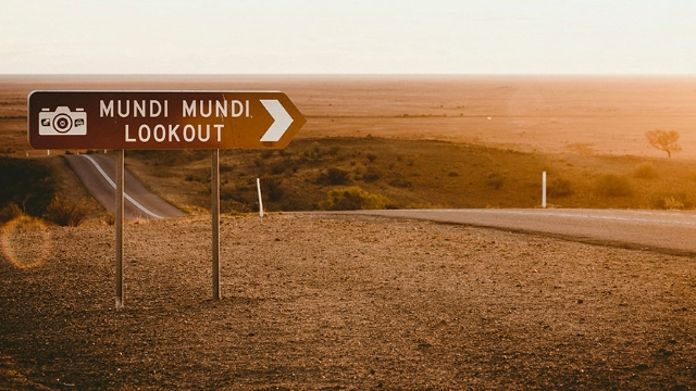 signpost saying mundi mundi lookout at the side of country road undulating through flat pastureland