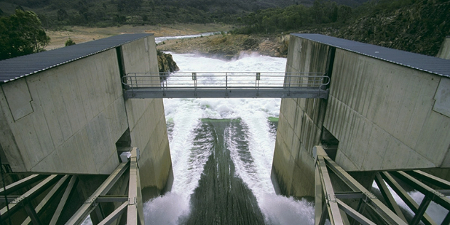  Two rectangular hydro station sections with a metal bridge between them over water rushing down into a river valley.