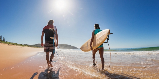 Two people walk along the beach carrying surf boards