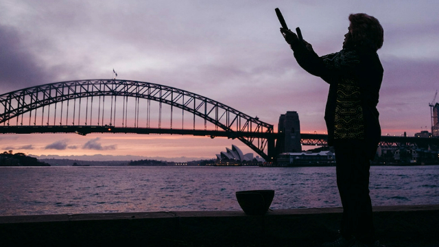 Aboriginal woman, Aunty Margret, storytelling at the Sydney Harbour shore, silhouetted by a sunrise.