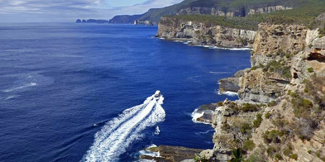  A panoramic view of the rocky, green topped cliffs of a peninsula, with a boat speeding along its coast.