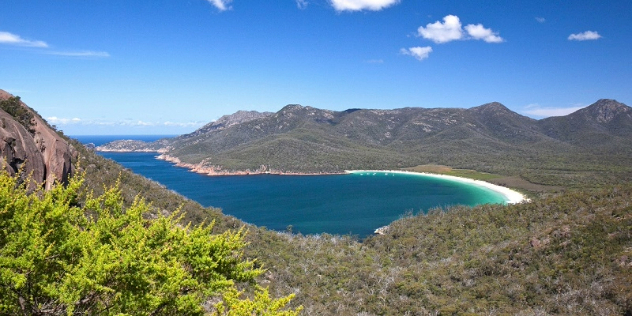 A panoramic view of a large bay with a white sand beach, surrounded by rainforest covered mountains.