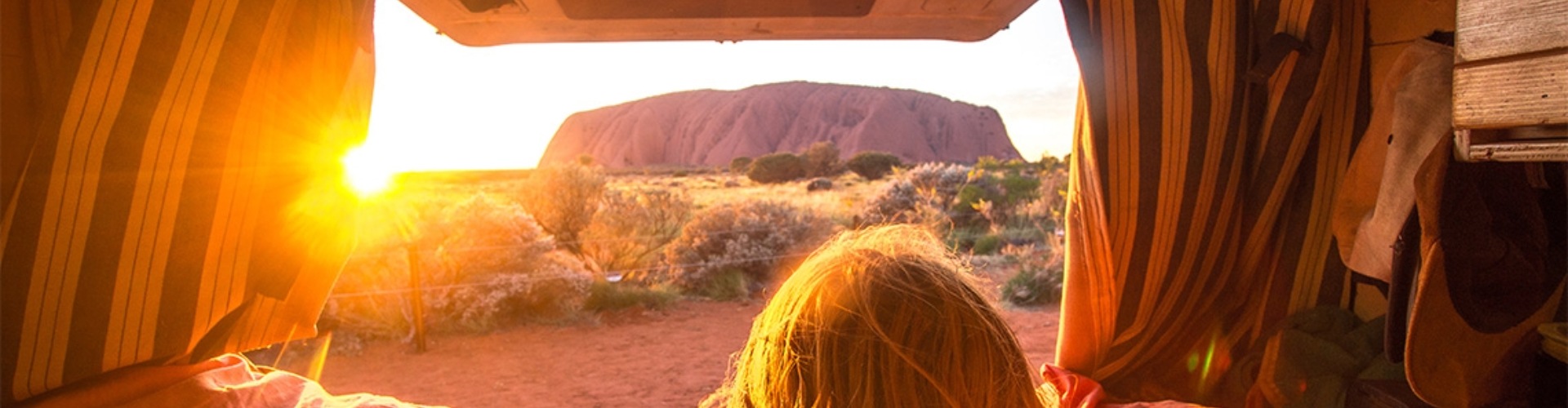 View of Ularu from a combi van A girl looking at Uluru from the back of her van at sunsset
