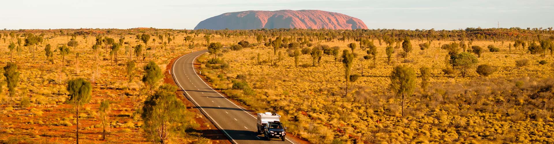 Landscape shot of a car and caravan on a road with Uluru in the background