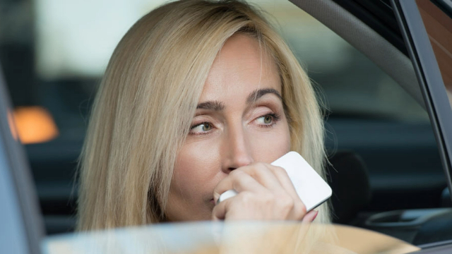 An upset woman sitting in a car holding a mobile phone